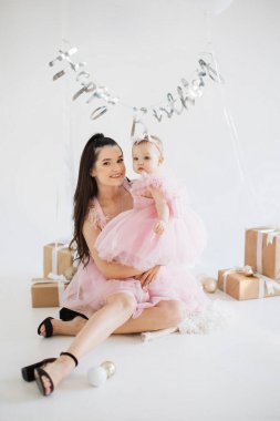 Gülümseyen beyaz kadın stüdyoda şirin kızıyla yerde oturuyor ve şenlikli bir atmosferle dolup taşıyor. İki çocuklu mutlu aile, tatlı bebeğin ilk doğum gününün anılarını kurtarıyor..