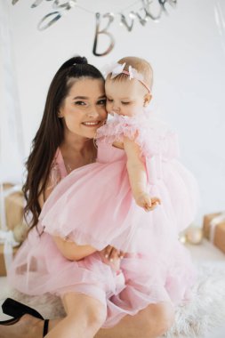 Gülümseyen beyaz kadın stüdyoda şirin kızıyla yerde oturuyor ve şenlikli bir atmosferle dolup taşıyor. İki çocuklu mutlu aile, tatlı bebeğin ilk doğum gününün anılarını kurtarıyor..