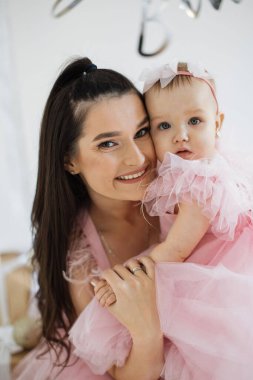 Genç anne ve küçük sevimli kızı hoş ve güzel dekore edilmiş stüdyo ortamının tadını çıkarıyorlar. Güzel kızlar birlikte doğum gününü kutluyorlar. Mutluluk ve kahkahalarla dolular..