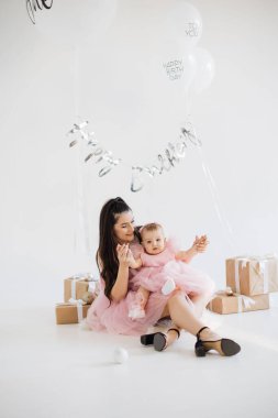 Gülümseyen beyaz kadın stüdyoda şirin kızıyla yerde oturuyor ve şenlikli bir atmosferle dolup taşıyor. İki çocuklu mutlu aile, tatlı bebeğin ilk doğum gününün anılarını kurtarıyor..