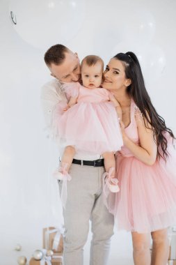 Şık kıyafetler içinde neşeli bir eş dekore edilmiş stüdyoda aşk dolu güzel bir kıza sarılıyor. Mutlu aile baba, anne ve küçük kız doğum günü kutlamalarını paylaşıyorlar..