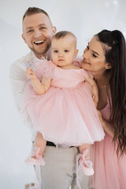 Şık kıyafetler içinde neşeli bir eş dekore edilmiş stüdyoda aşk dolu güzel bir kıza sarılıyor. Mutlu aile baba, anne ve küçük kız doğum günü kutlamalarını paylaşıyorlar..