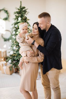 Kafkasyalı evli çift, sevimli küçük kızlarıyla rahat oturma odasındaki parlak Noel ağacının yanında oynuyorlar. Beyaz geyik oyuncağı veren bir adam bebeğini kucağında tutan çekici bir kadın..