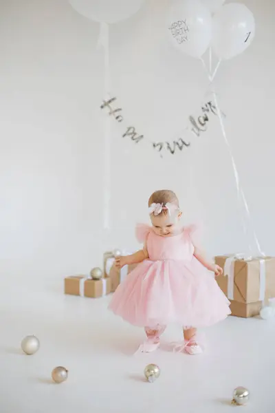 スタジオでプレゼントや風船の間に立っている間スタイリッシュな休日の服装で最初の誕生日を祝う素敵な少女 幼少期と祝賀の概念について — ストック写真