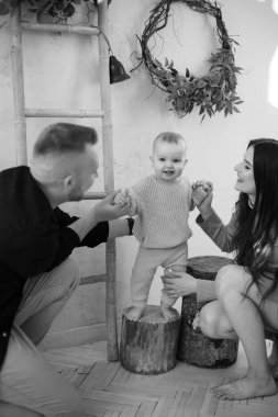 Anne ve babamın tahta bir kütüğün üzerinde duran küçük kızlarıyla vakit geçirdikleri siyah ve beyaz bir fotoğraf. Tasarımcı stüdyosunda yeni şeyler keşfeden meraklı bir bebek..