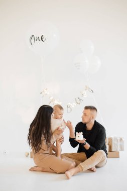 Kafkasyalı ebeveynler küçük kızlarını doğum günleriyle karşılamak için stüdyoda lezzetli pastalar, güzel hediyeler ve beyaz balonlar kullanıyorlar. Aile kavramı, yıldönümü ve kutlama.