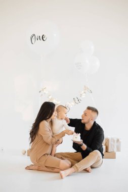 Kafkasyalı ebeveynler küçük kızlarını doğum günleriyle karşılamak için stüdyoda lezzetli pastalar, güzel hediyeler ve beyaz balonlar kullanıyorlar. Aile kavramı, yıldönümü ve kutlama.