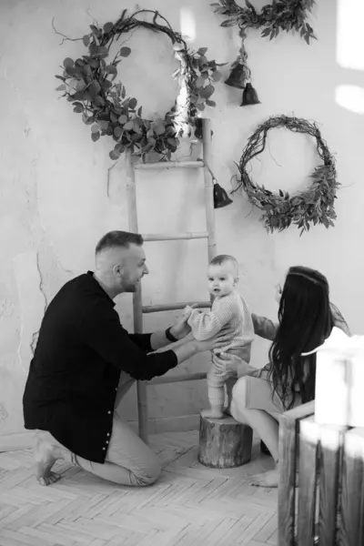 Tek renkli fotoğraf, şefkatli beyaz anne babaların oyuncu küçük kızını destekleyen kırsal tarzda dekore edilmiş bir stüdyoda. Aile kavramı, birliktelik ve boş zaman..