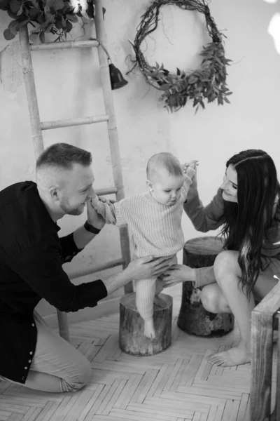 Anne ve babamın tahta bir kütüğün üzerinde duran küçük kızlarıyla vakit geçirdikleri siyah ve beyaz bir fotoğraf. Tasarımcı stüdyosunda yeni şeyler keşfeden meraklı bir bebek..