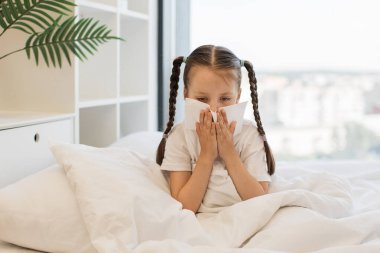 Kafkasyalı iki örgülü hasta kız rahat beyaz yatakta otururken beyaz dokuları burun çalıştırmak için kullanıyor. Evde grip sırasında hapşırmaktan yorgun düşmüş bir kadın çocuk..