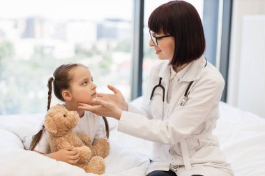 Gülen doktor, elinde oyuncak ayıyla lenf bezlerini incelerken nazikçe boynuna dokunuyor. Sevimli çocuk doktorlara korkuyla bakıyor ama tüm isteklerini yerine getiriyor. Sağlık tedavisi kavramı.