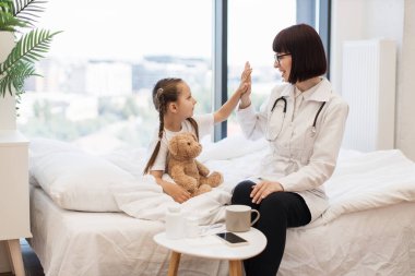 Güzel beyaz çocuk doktoru ve sevimli küçük kız yatakta otururken beşlik çakıyor. Doktor ve hastalardan oluşan dost canlısı bir ekip evdeki tedavi sonuçlarından memnun..