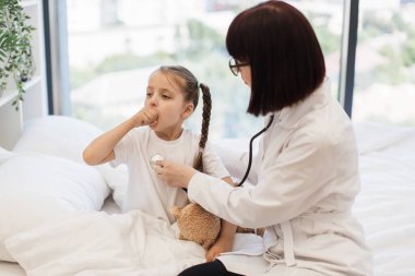 Steteskoplu küçük sevimli bir çocuğun nefes alan organlarını dinleyip öksürmesini isteyen nitelikli beyaz bir hemşire. Dost canlısı doktor küçük kızı muayene ediyor. Rahat yatak odasında tedavi için..