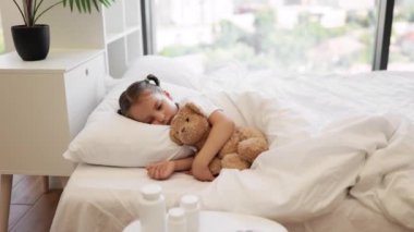 Beyaz yastıkların altında tatlı tatlı uyuyan beyaz tatlı beyaz kız ve oyuncak ayı arkadaşına sarılıyor. Evde iki örgülü güzel çocuk hastalık sırasında enerjisini geri kazanıyor..