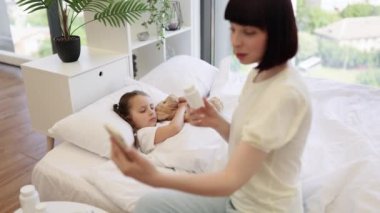 İlgilenen anne, doktorla modern akıllı telefondan iletişim kuruyor ve hasta kızının aldığı hapları gösteriyor. Tatlı kız yatakta uzanıyor ve yardım beklerken oyuncak ayıya sarılıyor..