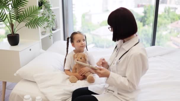 Wykwalifikowany Lekarz Siedzący Wygodnym Łóżku Obok Uroczej Chorej Dziewczyny Cyfrowym — Wideo stockowe