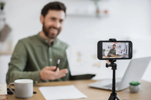 Masasında dizüstü bilgisayarla oturan ve akıllı telefon kamerasında mali raporunu gösteren beyaz adamın bulanık arkaplanı. Uzman finansör grafik grafikleri okumak ve yorumlamak hakkında video dersi veriyor.