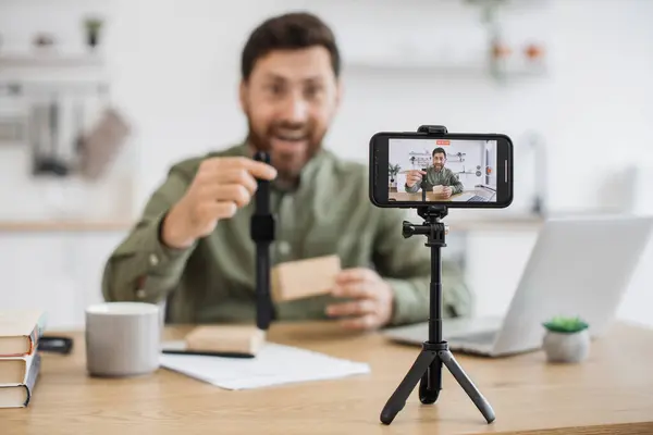 stock image Blurred background of impressed male showing off wonderful wristwatch with dark grey band during video blogging. Talkative delighted blogger answering followers questions about digital devices.