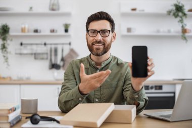 Modern akıllı telefonun canlı yayını sırasında takipçilerle geri bildirim paylaşan erkekleri etkileyen ilk kişi. Sakallı adam masada oturuyor ve yeni cep telefonunu işaret ediyor..