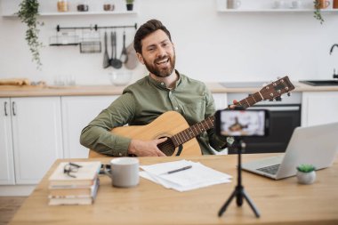 Evde oturup gitar çalma hakkında video dersi almak için akıllı telefon ve tripodu kullanan yetenekli bir müzisyen. Sosyal medya sanatsal deneyiminde takipçilerle paylaşan yakışıklı bir erkek blog yazarı.