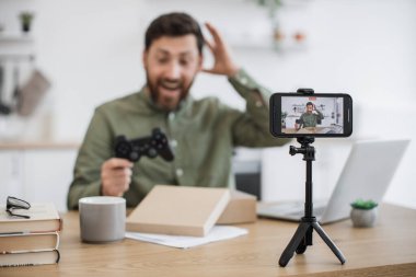 Canlı yayındayken elinde modern joystick ile yeni paketleri boks yaparken aşırı neşeli Kafkasyalı etkili. Çevrimiçi çalışan orta yaşlı adam bulanık arkaplanda sabit bir akıllı telefon ile çekim yapıyor..