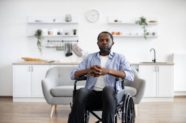 Modern dairenin açık planlı mutfağında dinlenirken kameraya gülümseyen Afro-Amerikan tekerlekli sandalye kullanıcısının portresini yakından çek. Günlük giysiler içinde neşeli genç erkek içeride zaman geçiriyor..