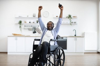 Modern stüdyo dairesinin rahatlığını kullanırken tekerlekli sandalyedeki yetişkin birinin joystick 'le el kaldırması. Kendini işine adamış bir oyuncu başarılı bir final sonrası zafer jestinden haz duyar..