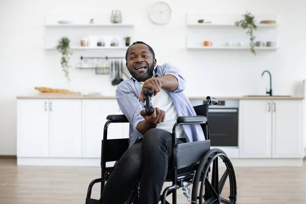 Close up view of african male gamer with mobility impairment with input devices in spacious kitchen in home interior. Joyous competitor honing skills in video games while pursuing enjoyable pastime.