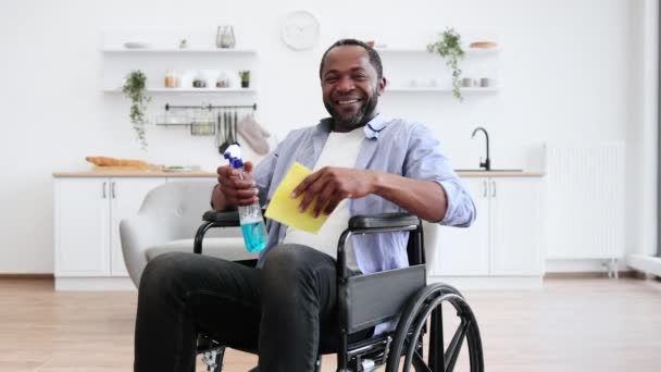 オープンプランのキッチンで車椅子に座っている間 障害を持った若いアフリカ系アメリカ人男性と ほこりを掃除するための黄色いスポンジ — ストック動画