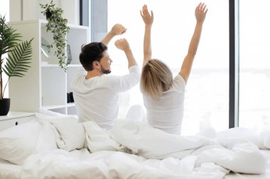 Beyaz tenli çiftin arka görüntüsü, gündelik giysiler içinde, her gece yataklarında uzuvlarını esnetiyorlar. Rahat aile babası ve kadın modern dairede güneşli bir güne başlıyorlar..