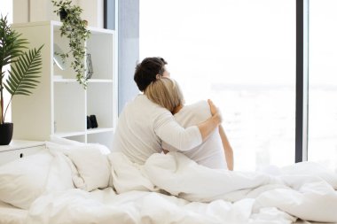 Beyaz tenli, sıradan giyinmiş, her gece sarılıp, parlak yatak odasında uyuyan bir çiftin arka görüntüsü. Rahat aile babası ve kadın modern dairede güneşli bir güne başlıyorlar..