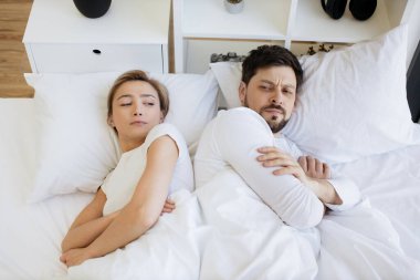 Beyaz yastığın üzerinde battaniyeyle uzanmış beyaz bir kadın ve kocası aydınlık yatak odasında uzanmış ona bakarken onu gücendirdi..