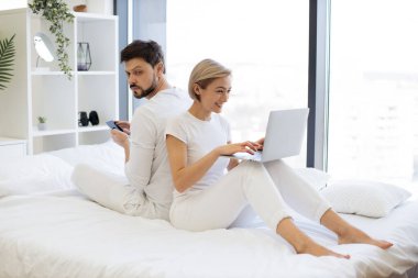 Neşeli şehvetli insanlar hafta sonları birlikte geniş bir dairede otururken sırt sırta oturuyorlar. Neşeli Kafkas ailesi kablosuz cihazlarda sosyal medyayı kaydırıyor.