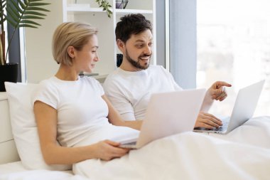 Güzel genç bir kadın yatakta oturuyor ve kocası ona tavsiyelerde bulunurken modern dizüstü bilgisayarla mesajlar yolluyor. Evli çifti sevmek evde dinlenerek teknik yaşam dengesini sağlıyor..