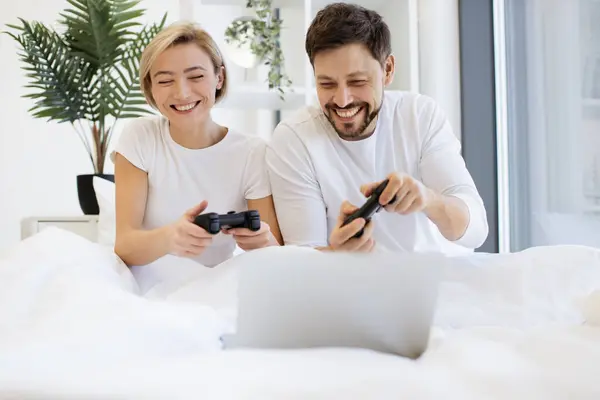 Cheerful amorous people accessing portable computer while spending time together playing video games in spacious apartment at weekend.