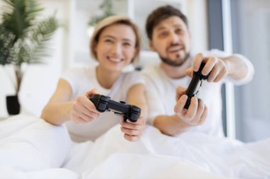 Evde battaniyenin altında yatarken video oyunu oynayan konsantre olmuş beyaz bir çiftin ellerine odaklan. Televizyonda gülümseyen adam ve kadın video oyununda yarışırken eğleniyor..