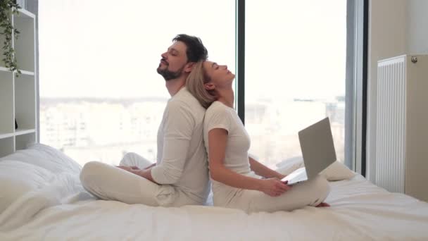 愛する夫婦は 自宅で休むテクノロジーライフバランスを達成しました ベッドに座り 現代のノートパソコンを使ってテキストメッセージを送る若い女性 夫がスマートフォンで背中に座っている間 — ストック動画