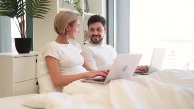 Güzel genç bir kadın yatakta oturuyor ve kocası ona tavsiyelerde bulunurken modern dizüstü bilgisayarla mesajlar yolluyor. Evli çifti sevmek evde dinlenerek teknik yaşam dengesini sağlıyor..