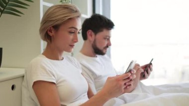 Modern dairenin yatak odasındaki rahat yorganın altında otururken akıllı telefonlar kullanarak internette sörf yapan Kafkasyalı karı koca. Sosyal medya üzerinden dijital aygıtlar aracılığıyla ağ kurmakla meşgul eşler.