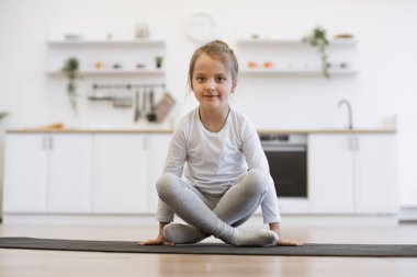 Yoga yapan güzel bir kızın ön görüntüsü, vinç egzersizi, bakasana pozu spor giysisi, kapalı alanda, beyaz mutfak arka planında spor giyinme..