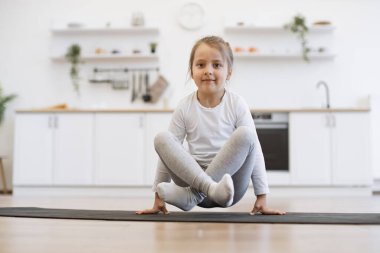 Yoga yapan güzel bir kızın ön görüntüsü, vinç egzersizi, bakasana pozu spor giysisi, kapalı alanda, beyaz mutfak arka planında spor giyinme..