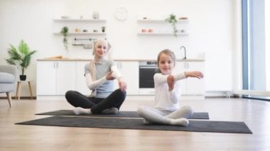 Yoga minderindeki sıska müslüman kadın küçük bir kızla çalışırken kollarını esnetiyor. Spor giyim sektöründe genç bir ebeveyn ve kız spor yaparken eğleniyor..