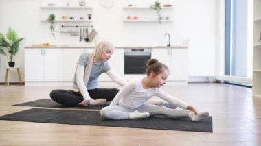 Yoga minderinde, kollarını ve bacaklarını esneten, eğitimdeyken gözleri kapalı, sıska Müslüman bir bayanın yan görüntüsü. Spor giyim sektöründe genç bir ebeveyn ve kız spor yaparken eğleniyor..