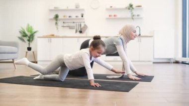 Aktif sıska Müslüman bayan ve kızı spor kıyafetleriyle evdeki minderlerin üzerinde denge masasında poz veriyorlar. Güzel anne ve kız arkadaşı mutfakta yoga egzersizi yapıyorlar..