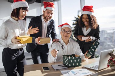 Noel Baba şapkalı bir grup çok uluslu iş arkadaşı, Asyalı erkek yöneticiye Noel hediyesi kutuları veriyor. Şu anda boks masasında oturuyorlar ve kameraya şaşkınlıkla bakıyorlar..