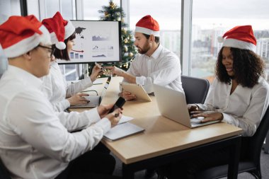 Noel Baba şapkalı çok ırklı iş arkadaşları plazma ekran ve Noel süsleme ağacıyla toplantıda. Yakışıklı sakallı takım lideri bayan meslektaşımla mali durumu tartışıyor.