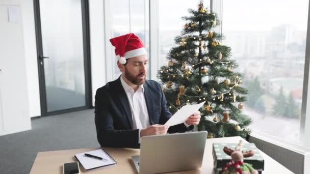 クリスマスツリーのバックグラウンドでオフィスからプレゼンテーションしながら グラフィック素材でペンを指して自信を持った大人 現代技術を用いた統計解析を提供する集中労働者 — ストック動画