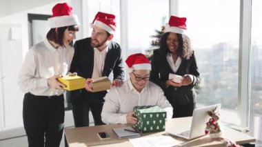 Gizli Noel Baba. Noel Baba şapkalı gülümseyen Asyalı işadamı, yanında duran çok uluslu meslektaşlarından aldığı bir Noel hediyesini açıyor. Yeni Yıl Arifesi.