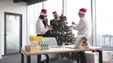 Çok ırklı bir grup iş arkadaşı Noel ağacı süsleyerek başlangıç ofisine şenlik süsü koyuyorlar. Mutlu insanlar kış tatilini kutlamak için kostüm ya da ışıklarla eğleniyorlar..