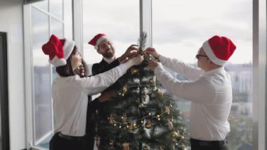 Çok ırklı bir grup insan Noel ağacı dekorunu şenlik ofisine yerleştiriyor, kış mevsimi geleneğine hazırlanıyorlar. Noel tatili için kostüm takılan işyeri dekorasyonu.